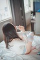 A woman sitting on a bed drinking from a bottle.