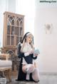 A woman dressed as a nun sitting on the floor holding a book.