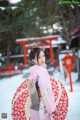 A woman in a pink kimono holding an umbrella in the snow.