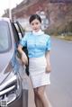 A woman in a blue shirt and white skirt standing next to a car.