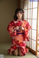 A woman in a red kimono sitting on the floor.