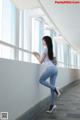 A woman in a white shirt and blue jeans leaning against a wall.