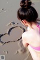 A little girl in a pink bikini writing a heart in the sand.