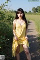 A woman in a yellow dress standing on a dirt road.