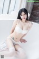 A woman in a white lingerie sitting in a bathtub.