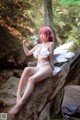 A woman in a white bikini sitting on a tree branch.