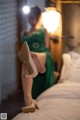 A woman in a green dress sitting on a bed.