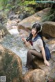 A woman sitting on a rock in a stream.