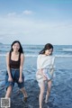 Two young women walking on the beach near the ocean.